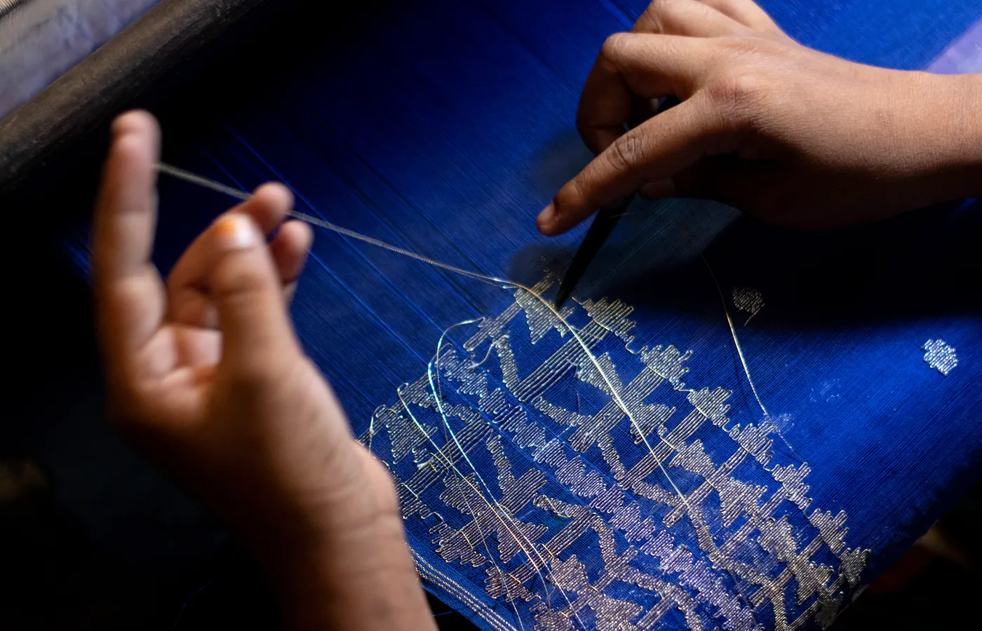 A weaver's hands lifting the pattern threads on a Jamdani loom